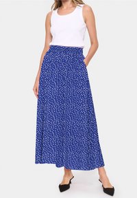 Modrá maxi sukně s bílými puntíky, elastickým pasem, bočními kapsami a volným materiálem. Kombinována s bílým tílkem a černými muly.