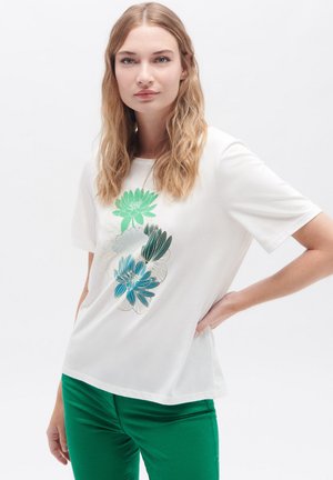 T-shirt bianco a maniche corte con un design floreale arricchito da accenti verdi e blu, abbinato a pantaloni fitted verdi. Texture liscia.