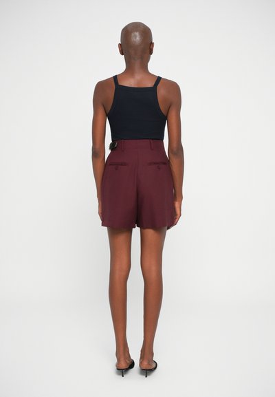 Shorts ajustés bordeaux avec poches arrière, portés avec un top sans manches noir. Tissu lisse, longueur mi-cuisse et détails de design minimalistes.