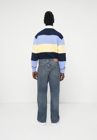 Maglione a righe in blu chiaro, giallo e blu navy; abbinato a jeans in denim blu chiaro con patch logo e vestibilità rilassata.