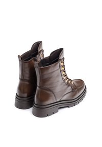 Bottines en cuir marron avec une finition lisse, des œillets dorés, des lacets robustes et une semelle en caoutchouc texturée pour une bonne adhérence.