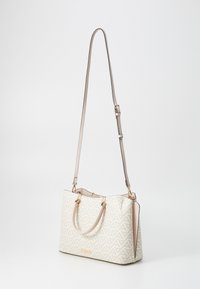 Beige håndtaske med geometriske mønstre, guldkvadrat og en aftagelig skulderrem. Har en glat overflade og en struktureret form.