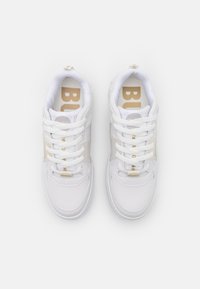 Paire de baskets basses blanches avec des lacets blancs et un marquage beige sur les semelles intérieures, vue de dessus sur fond blanc.