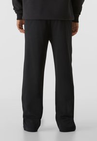 Pantaloni de trening negri din material moale, cu croială lejeră, picioare drepte și talie elastică cu tiv reiat. Fără modele sau accente vizibile.