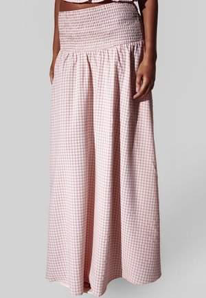 Kvinde iført en højtaljet, lyserød og hvid ternet lang nederdel med smocket talje og en matchende cropped top mod en neutral baggrund.