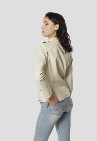 Krémová kožená motocyklová bunda so zipsovými manžetami, priliehavým strihom a jemnými detailmi šitia. Doplnok k svetlomodrým rifliam.