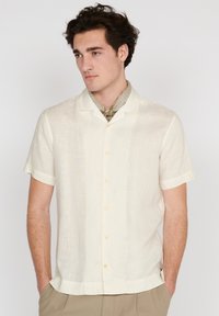 Camisa de botones de manga corta, de color crema, en una tela ligera con una textura sutil. Presenta un cuello relax y botones a juego.