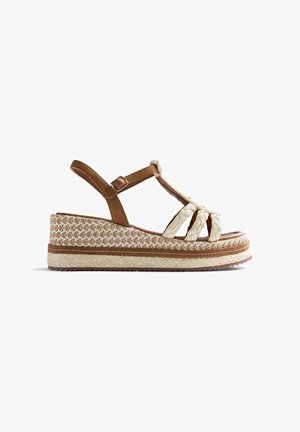 Sandalia de cuña con tiras trenzadas beige, correa ajustable marrón en el tobillo y suela plataforma tejida con patrón.
