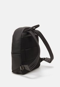 Sac à dos noir en matériau synthétique texturé. Bretelles rembourrées, accents en maille et poignée supérieure. Fermeture zippée et boucles réglables.