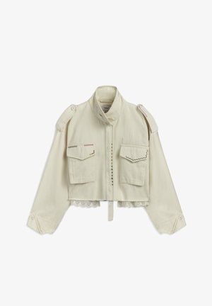 Veste courte en crème en toile avec deux poches avant, couture décorative, boutons sur les épaules et dentelle au niveau de l'ourlet.
