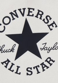 Logo dei Converse All Star nero con una stella a cinque punte centrale e le firme "Chuck Taylor" su sfondo di tessuto crema.