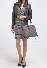 Gray leather handbag with a structured shape, logo detail, and dual handles. Worn with a patterned dress and black high heels.