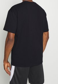 Camiseta negra de manga corta, cuello redondo, corte regular, hecha de algodón, textura suave, diseño liso, sin patrones ni gráficos visibles.