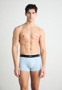 Világoskék boxer nadrág fekete derékkal, amelyen a márkaneve látható. Simább textúra, testhezálló design és combközép hosszúság.