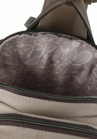 Innenraum einer Ledertasche mit einer weichen, strukturierten Oberfläche in hellem Creme. Enthält Reißverschlusstaschen und ein gemustertes Futter mit hellgrauem Text.