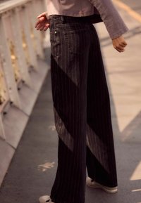 Laiad mustad pinstripe teksad, mis on valmistatud denimist; omadused hõlmavad tagakotte, kinnitatud vööd ja sileda tekstuuri kergelt läikiva pinna jaoks.