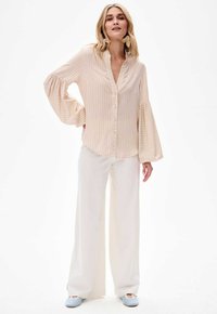 Jasnoróżowa bluzka w paski z obszernymi rękawami, zapinana na guziki z przodu, zestawiona z szerokimi białymi spodniami i jasnoniebieskimi balerinami.