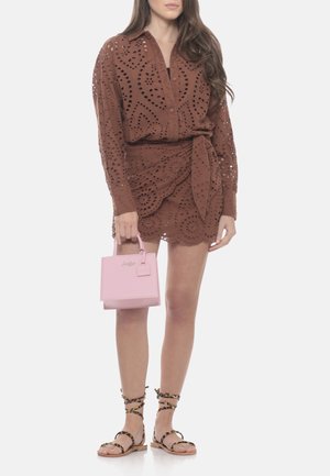 Donna che indossa una camicetta marrone con bottoni a occhiello e una gonna a portafoglio abbinata, tiene una piccola borsa rosa e indossa sandali con stampa leopardata e cinturini.