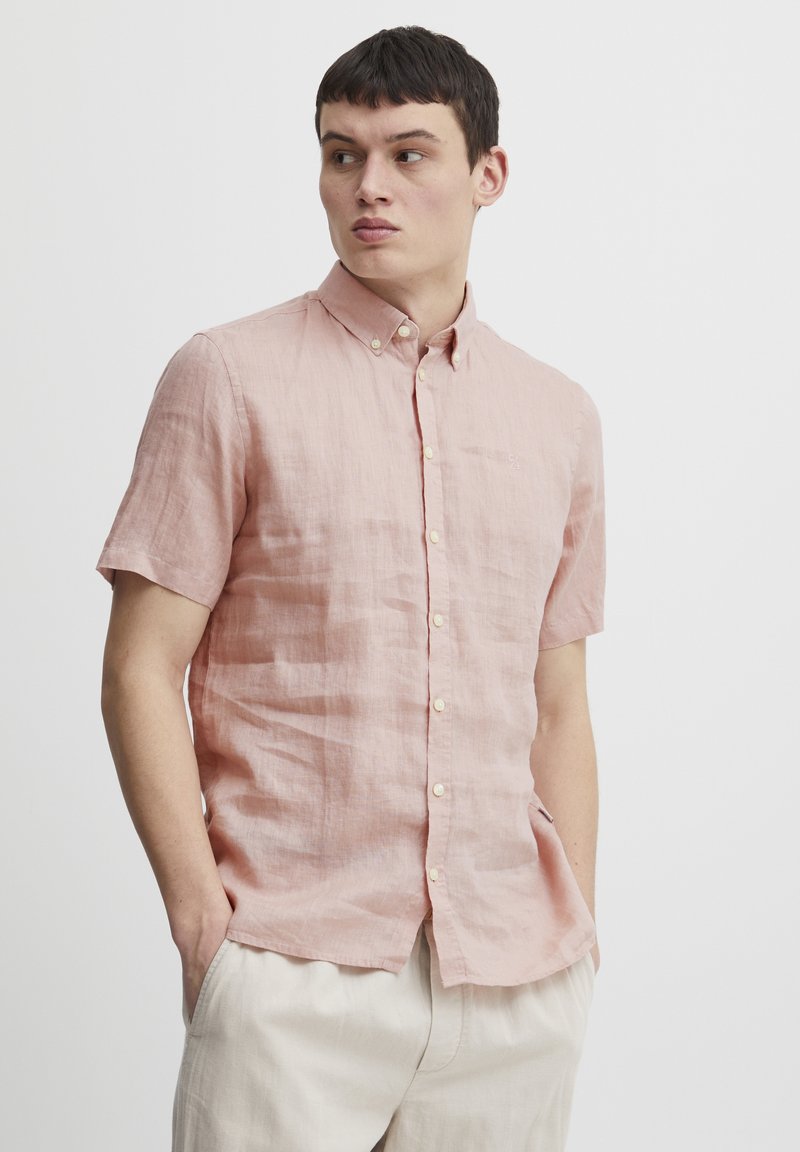 Lichtroze linnen overhemd met korte mouwen, een button-down kraag, een voorpaskant en subtiele textuur, gecombineerd met lichtbeige broek.