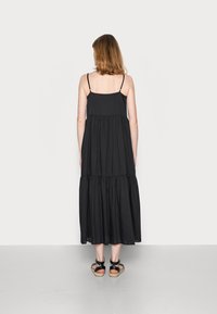 Robe maxi noire à volants avec des fines bretelles, en tissu fluide et à coupe décontractée. Dispose d'un détail de couture à la taille et est de longueur cheville.