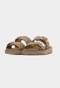 Paire de sandales beiges avec deux brides réglables, boucles dorées, petites décorations cloutées et semelles épaisses à rainures.