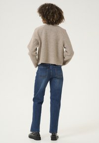 Beige kortärmad tröja med strukturerad stickning, tillsammans med rakbenade mörkblå jeans och svarta skor, sedd bakifrån.