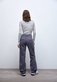 Grå og hvid stribet langærmet top med tætsiddende talje, parret med løse grå cargo bukser med sidelommer og en afslappet pasform.