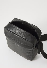 Black leather crossbody bag with a textured finish, zip closure, and a logo detail. Features adjustable strap and a compact shape.