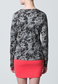 Šedá košile s dlouhým rukávem s černým skvrnitým vzorem, doplněná o strukturovanou, přiléhavou korálovou sukni, která zdůrazňuje kontrast barev a stylů.