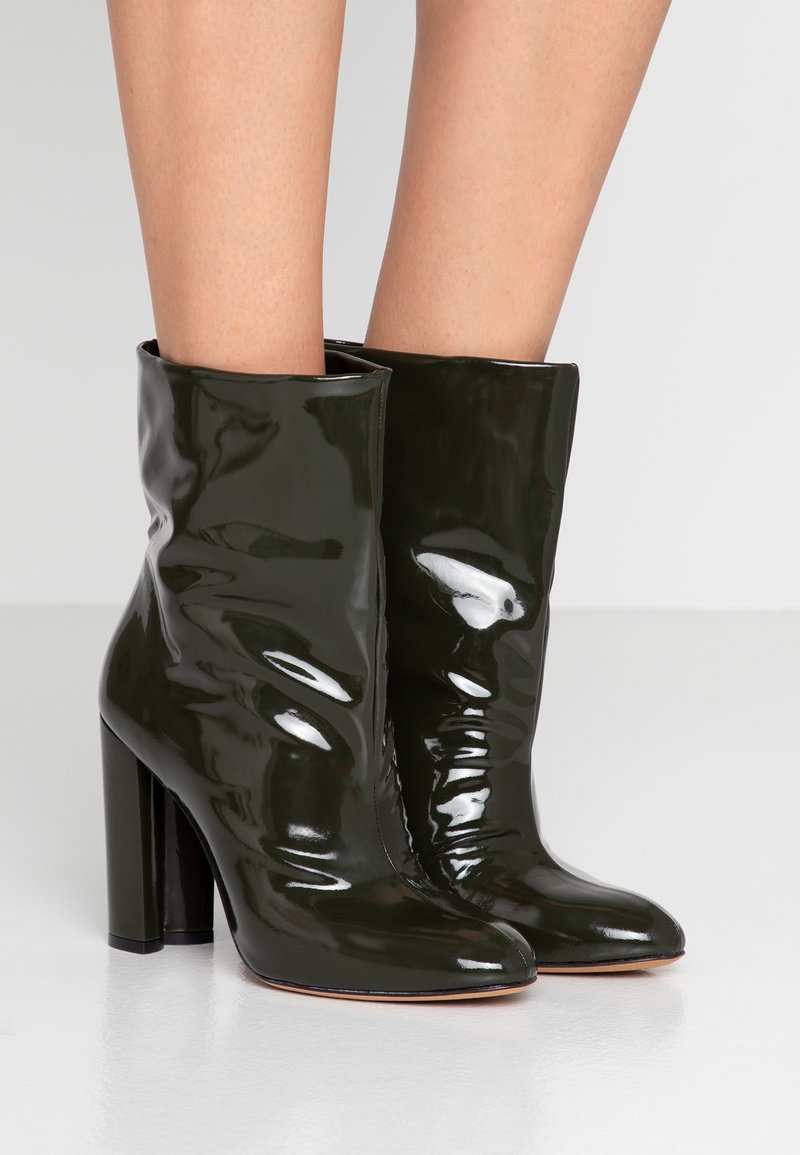 Bottes courtes en cuir verni vert avec une finition brillante, une forme élégante, des bouts pointus et des talons hauts carrés, présentant un design légèrement froncé.