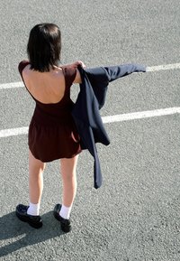 Rochie ajustată bordo cu spatele deschis, asortată cu o jachetă bleumarin purtată pe umăr. Pantofi cu platformă negri și șosete albe. Fundal din asfalt.