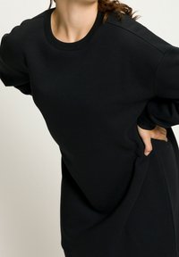 Sweatshirt noir en tissu doux, avec un col rond et une coupe décontractée. Les manches ont un design légèrement bouffant.