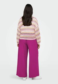 Maglione lavorato a maglia con righe multicolori su un paio di pantaloni a gamba larga color lilla, caratterizzati da un tessuto testurizzato. Scarpe bianche casual.
