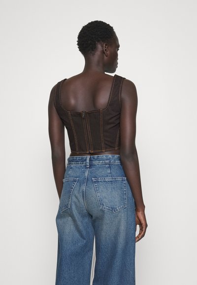 Haut court marron avec des coutures orange contrastantes et une fermeture éclair, associé à un jean en denim bleu loose avec des poches arrière.