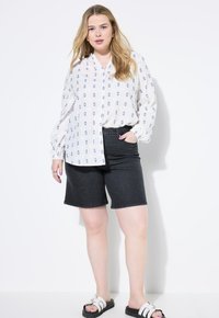 Witte langearmige blouse met blauwe ruitpatronen, gecombineerd met donkere denim shorts en zwarte slide sandalen.