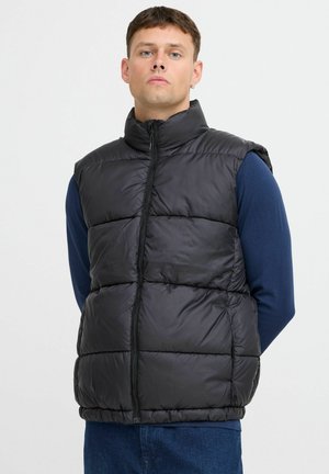 Zwarte puffer vest met een hoge kraag, ritssluiting en een gequiltde textuur, gedragen over een blauwe lange mouwen shirt. Geen mouwen of zakken zichtbaar.