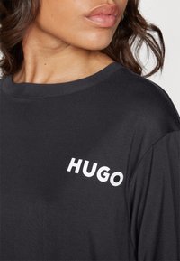 T-shirt noir en tissu doux, avec un col rond et un logo blanc "HUGO" bien visible sur le côté gauche de la poitrine.