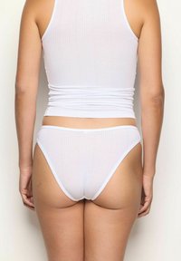 Top corto a coste bianco e bikini abbinato con un design aderente. Il tessuto ha una texture liscia, con spalline sottili e gambe a taglio alto.
