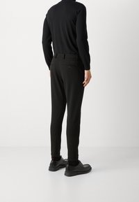 Czarne dopasowane spodnie z nogawkami zwężanymi ku dołowi, posiadające tylne kieszenie i gładki materiał, w połączeniu z czarnymi butami i czarną bluzką z długim rękawem.