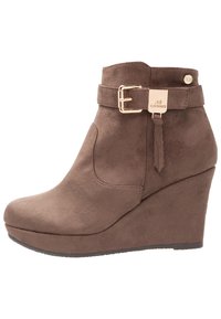 Stivaletti a zeppa in suede marrone con dettaglio della fibbia e superficie texture. Punta arrotondata e design liscio e senza giunture.