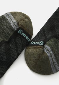 Pair of socks featuring an olive green and black design, highlighting textured patterns and a logo in blue stitching along the cuff.