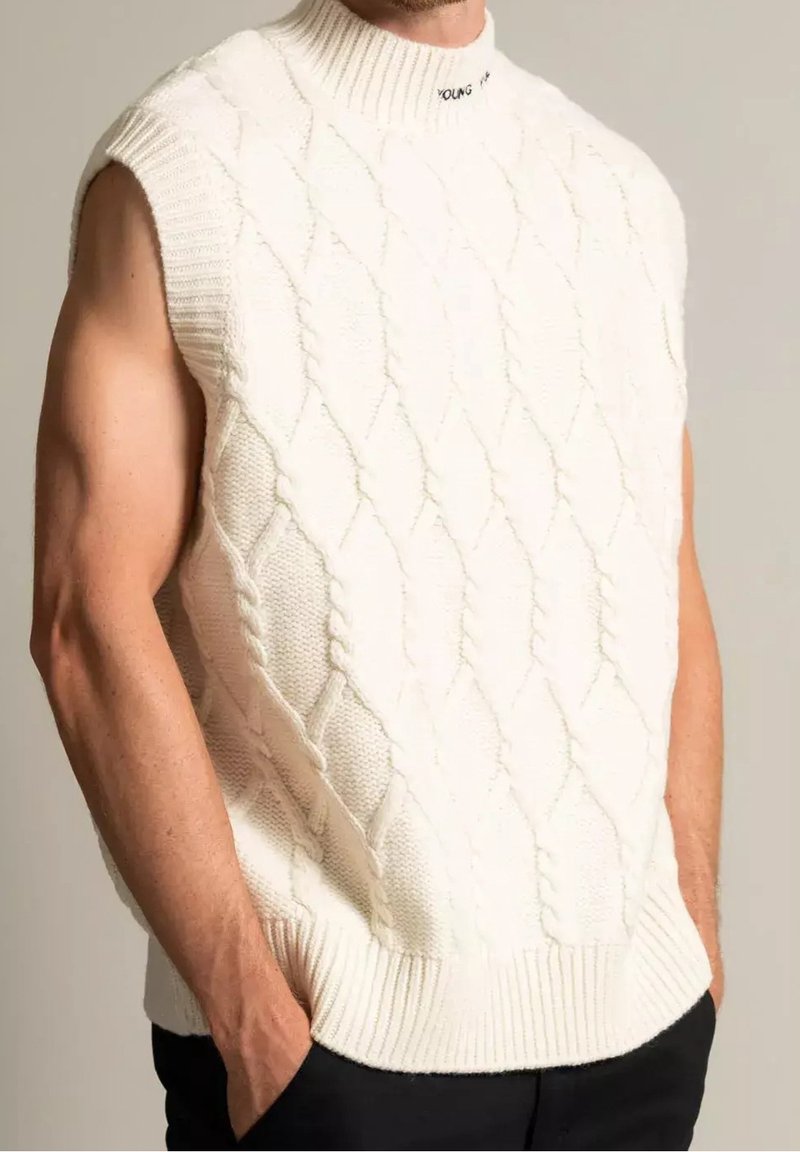 Bílý pletený bezrukávový svetr s vysokým ribovým límcem, který má strukturovaný diamantový vzor a nápis "YOUNG" na límci.