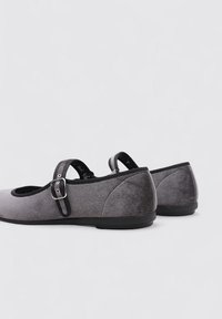 Zapatos Mary Jane de ante gris con punta redondeada, ribete negro y correa con hebilla. Suelas planas con una textura suave y características de diseño mínimas.