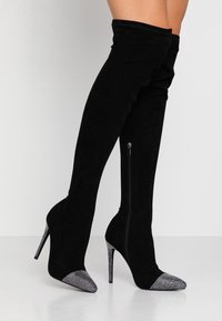 Musta mokkanahka yli polven saappaat, joissa on korkea stiletto-korko. Hopeiset strassikoristeet kärjessä ja sivu vetoketju.