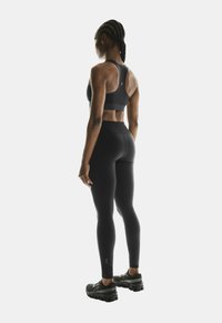Schwarzer Sport-BH und Leggings aus einem glatten, dehnbaren Material, mit einem hohen Bund und strukturierten Details an den Schuhen.