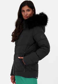 Giacca a vento nera con cappuccio in pelliccia sintetica, texture trapuntata, polsini a coste e tasche con zip. Accentuata da un logo sulla manica.