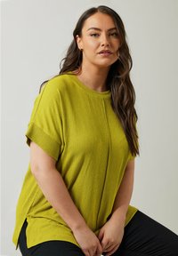 Top corto de color verde lima, hecho de una tela texturizada, con cuello redondo y aberturas en los laterales, combinado con pantalones negros.