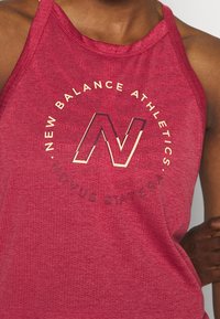 Camiseta deportiva roja sin mangas con una textura suave y transpirable, que presenta un destacado logo dorado con la "N" y texto circular de la marca impreso en el frente.