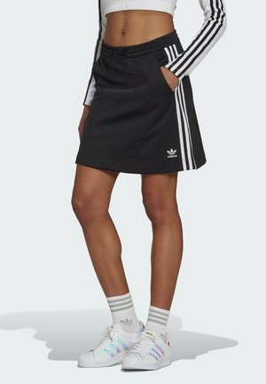 Gonna sportiva nera con cintura elastica e tasche laterali, caratterizzata da accenti bianchi a tre strisce e un logo Adidas all'orlo.