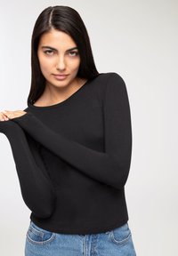 Czarny top z długim rękawem, wykonany z miękkiego materiału, z okrągłym dekoltem, z dopasowanymi rękawami i skróconym fasonem, w połączeniu z jasnymi dżinsami.